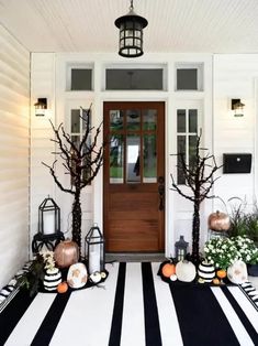 front porch decorated for halloween with black and white striped rug, pumpkins, trees and lanterns