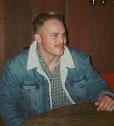 a man sitting at a wooden table with a blue jacket on