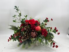 a bouquet of red flowers and greenery in a silver vase on a white background