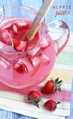 a pitcher filled with liquid and strawberries on top of a cloth next to a wooden spoon