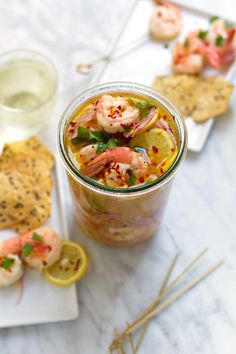 a glass jar filled with shrimp and lemonade next to crackers on a plate