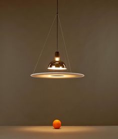 an orange sitting in front of a light hanging from it's side on a table