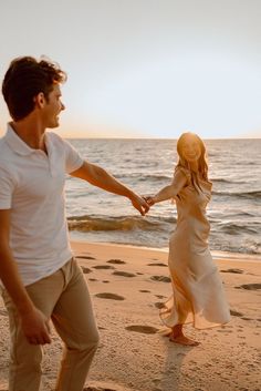 a man and woman holding hands while walking on the beach near the ocean at sunset