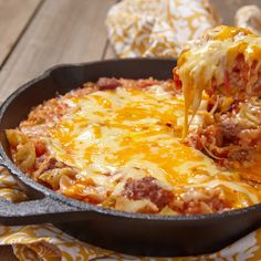 a skillet filled with lasagna and cheese on top of a wooden table