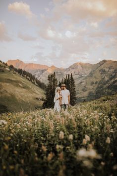 a man and woman standing on top of a lush green hillside