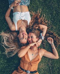 two women laying on the grass with their arms around each other and looking up at the camera