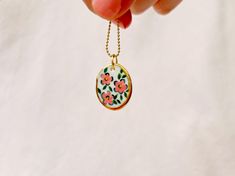 *Please note this listing is for the pendant only, does not include necklace pictured* Hand-Painted Porcelain Floral Pendant with Gold Lustre & Gold-Plated Brass Link: Material: Fine porcelain with hand-painted floral design accented with gold lustre. Link: Gold-plated brass. Care: Handle with care; clean with a soft cloth to preserve the gold lustre and plating Whether you're looking for a unique gift or a special piece to elevate your own jewellery collection, this pendant is a perfect choice. Hand Painted Enamel Round Pendant Necklace, Hand Painted White Enamel Necklace, Handmade Enamel Flower Pendant Necklace, White Enamel Hand Painted Necklace, White Hand Painted Enamel Necklace, Artisan Hand Painted White Necklace, Artisan Hand Painted White Necklaces, Artisan White Hand Painted Necklaces, Hand Painted White Pendant Jewelry