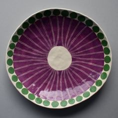 a purple bowl with green dots on the rim and white circle in the center, sitting on a gray surface