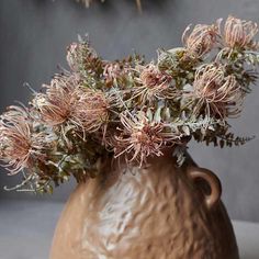 a brown vase filled with lots of flowers on top of a wooden table next to a wall