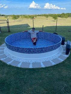 a man sitting on top of a large blue pool in the middle of a field