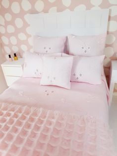 a pink bed with white polka dot wallpaper and two pillows on the headboard