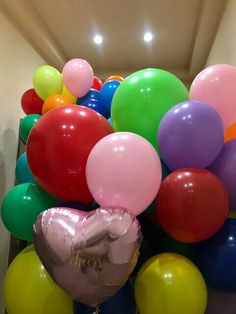 a bunch of balloons that are sitting on the ground in front of a wall with a heart shaped balloon attached to it