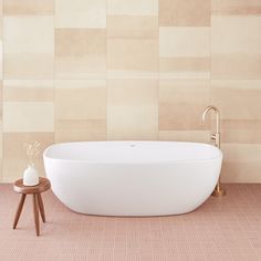 a white bath tub sitting on top of a tiled floor next to a wooden stool