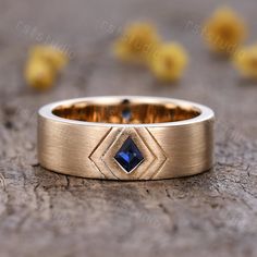 a gold wedding band with a blue sapphire stone in the center on a wooden surface