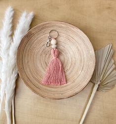 a pink tasseled keychain sitting on top of a wooden plate next to feathers