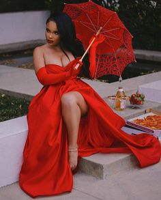 a woman in a long red dress sitting on steps with an umbrella over her head