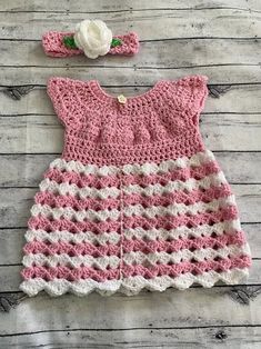 a pink and white crocheted dress with a flower on the headband is laying on a wooden surface