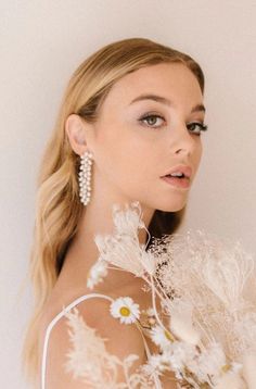 a woman with long blonde hair and earrings on her shoulder is holding flowers in front of her face