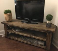 a flat screen tv sitting on top of a wooden stand next to a potted plant