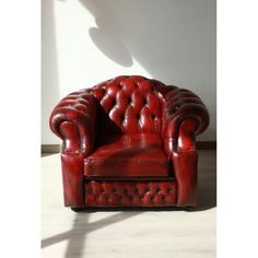 a red leather chair sitting on top of a hard wood floor next to a white wall