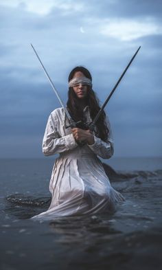 a woman with two swords standing in the water