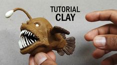 two hands holding a clay model of a fish with its mouth open and teeth out