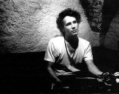 black and white photograph of a man sitting in front of a rock wall with his hands on the ground