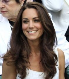 a woman sitting in the stands at a tennis match wearing a white dress and smiling