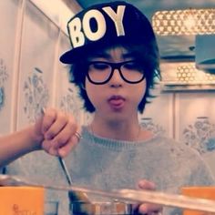 a boy wearing glasses and a hat making a funny face while eating food from a bowl