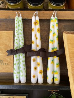 four candles with flowers painted on them are tied to a wooden shelf in front of jars