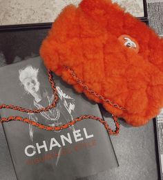 an orange purse sitting on top of a black table next to a book and chain