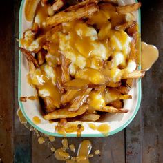 a bowl filled with french fries covered in cheese and sauce on top of a wooden table