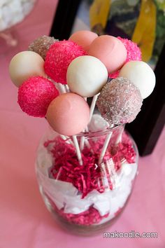 some cake pops are in a glass vase on a pink tablecloth with red and white sprinkles