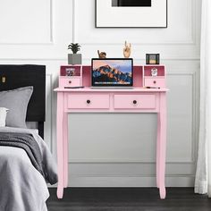 a pink desk with two drawers and a laptop on it in front of a bed