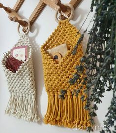 two crocheted purses hanging from hooks on a wall next to a potted plant