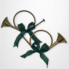 two brass trombones with green bows tied around them on a white surface, one is in the shape of an oar