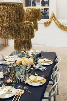 a table set with plates, silverware and gold sequins hanging from the ceiling