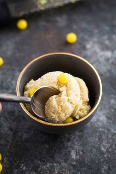 a bowl filled with ice cream and yellow candies next to a hand holding a spoon