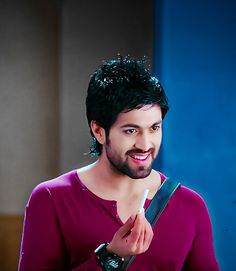 a man with black hair is smiling and holding a toothbrush in his hand while wearing a purple shirt