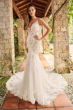 a woman in a white wedding dress standing on a brick walkway with her hands on her hips