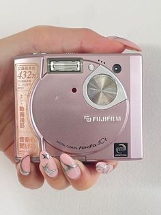 a woman's hand holding a pink camera in front of her face and nails