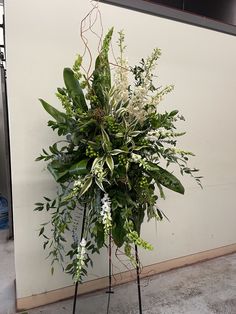 a plant stand with white flowers and greenery on the floor next to a wall