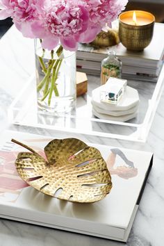 pink flowers are in a vase on a tray next to a book and some candles