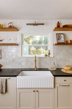 a kitchen with white cabinets and black counter tops is pictured in this image, there are shelves on the wall above the sink