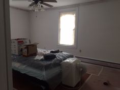 an empty room with a bed, ceiling fan and boxes on the floor in front of it