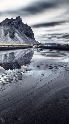 a mountain is reflected in the water on a cloudy day with low tide coming in