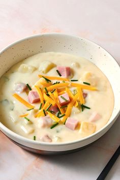 a bowl of soup with ham, cheese and green onions on the side next to a spoon