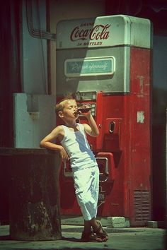 a young boy standing in front of a coca cola machine