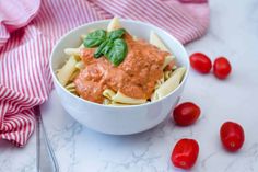 a white bowl filled with pasta covered in sauce and garnished with green leaves