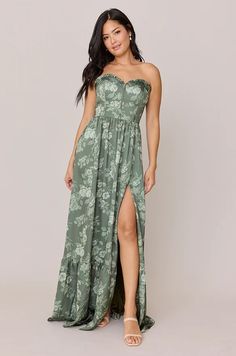 a woman wearing a green floral print dress with thigh high slits and an asymmetrical bustier